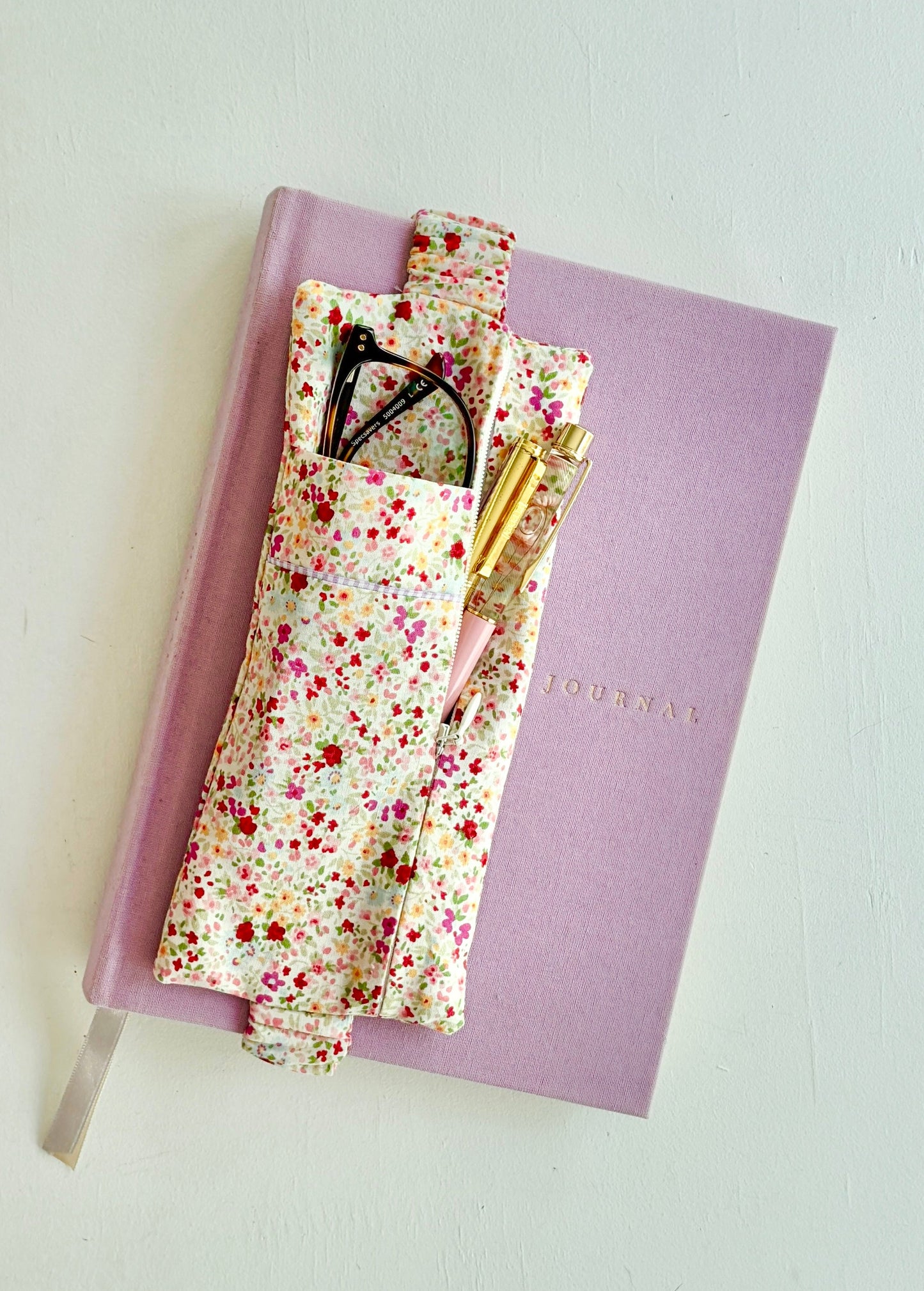 Pink notebook with floral cover and stationery items on a light gray background