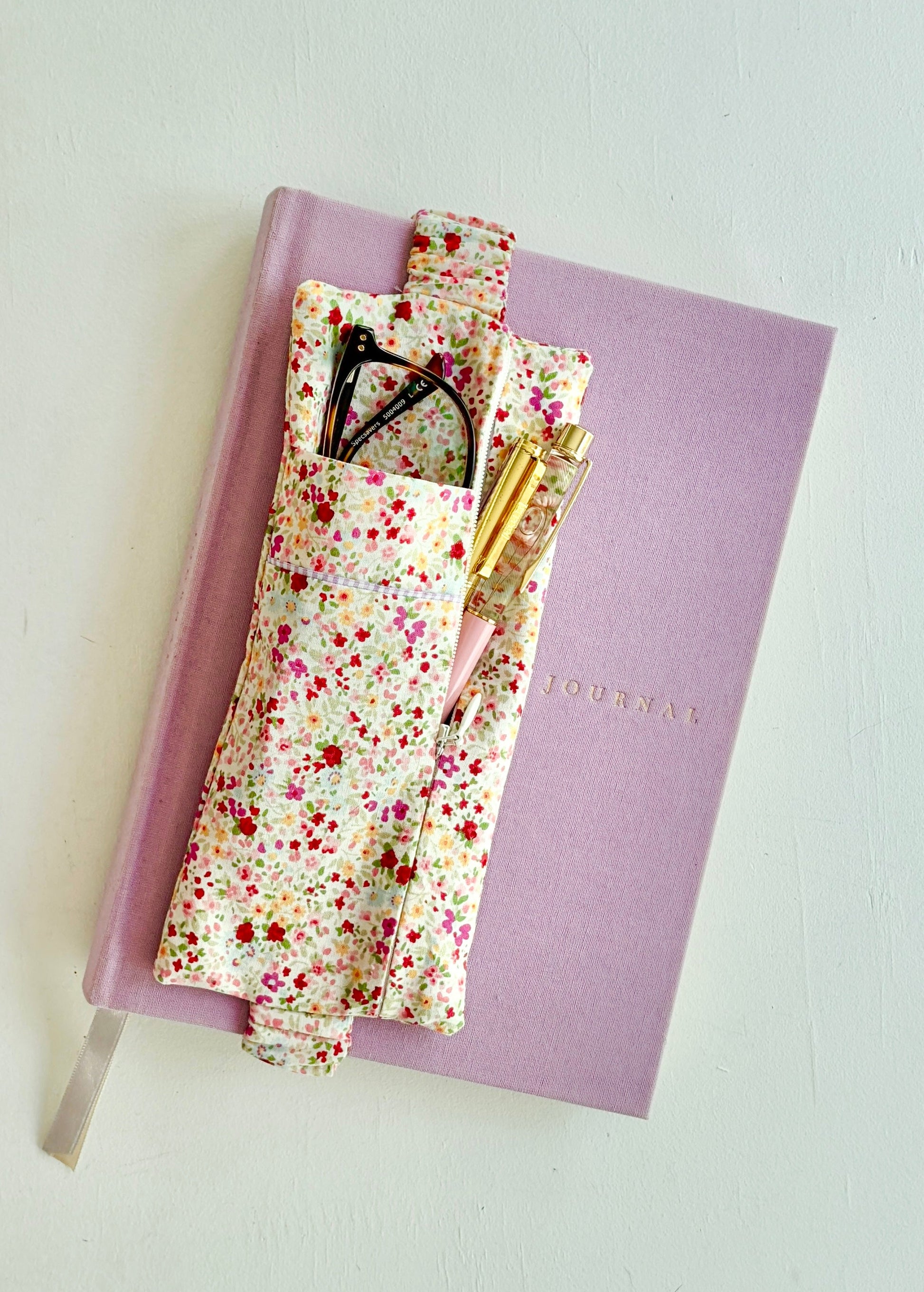 Pink notebook with floral cover and stationery items on a light gray background